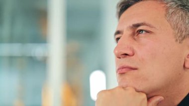 Koyu renk gömlekli düşünceli bir işadamı modern ofis ortamında dikkatlice düşünür. Ciddi bir ifadeyle başarılı bir erkek uzman, dikkatle dinliyor. Yansıtıcı profesyonel.