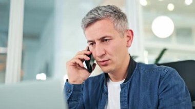 Mavi kot ceketli ve beyaz tişörtlü odaklanmış işadamı, modern bir ofiste özenle çalışıyor, ciddi bir telefon görüşmesi yapıyor, proje detaylarına odaklanıyor..