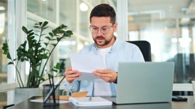 Endişeli iş adamı ofis masasında hayal kırıklığı yaratan bir belge okuyor. Hüsrana uğramış tepkisi finansal sorunları ya da beklenmedik kötü haberleri gösteriyor. Stres ve hayal kırıklığı yaratıyor..