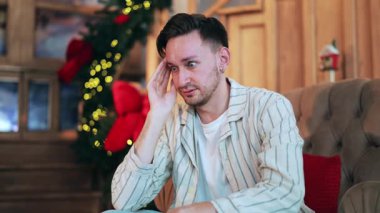 Genç bir yetişkin sıkıntı yaşıyor, tatil sezonunda endişeleniyor, kanepede oturuyor. Üzüntü, hayal kırıklığı, gösterişli bir dekorasyon. Zihinsel sağlık sorunları herkesi etkileyebilir..