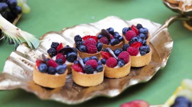 Zarif altın tepside sunulan taze böğürtlen ve kremayla süslenmiş mini meyveli turtalar. Hoşgörülü tatlı ikramlar neşeyi, mutluluğu ve tatmini çağrıştırır.