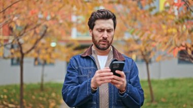 Sonbaharda açık havada telefonla yoğun baş ağrısı çeken bir birey. Dijital gerginlikten kaynaklanan rahatsızlık ve acı. Sağlık ve refah teknolojik kullanımdan etkileniyor, sıkıntıları ifade ediyor.