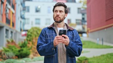 Bireyler mobil cihazlarla etkileşime girerken keyif ve memnuniyet hissederler. İnsan gülümser, akıllı telefondan içeriğe bakar, teknolojiyle olumlu bir bağlantı kurar. Kentsel arka plan şehir hayatı.