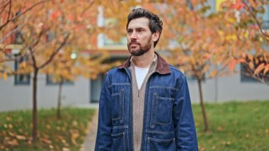 Olgun adam sonbahar ağaçlarının arasında duruyor, özgüvenini ve mutluluğunu ifade ediyor. Kameraya parlak bir şekilde gülümsüyor, dışarıda olumlu duygular taşıyor. Sevinç ve memnuniyet büyüleyici ve rahatlatıcı bir atmosferle dolu..