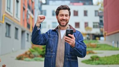 Yetişkinler, akıllı telefondan içeriği gördükten sonra başarıyı kutlayarak muazzam bir sevinç ve heyecan ifade eder. Açık şehir ortamı zafer anı için dinamik bir zemin sağlar. Neşeli hissediyorum