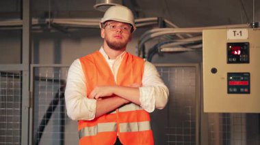 Profesyonel mühendis, sanayi ortamında kollarını kavuşturarak güvenle ayakta duruyor. Teknik görevler ve denetim için hazır. Nitelikli işgücü ve endüstriyel güvenliği temsil ediyor.