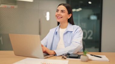 Genç profesyonel kadın dizüstü bilgisayarda yazarken zevk ve memnuniyet hissediyor. Modern ofiste verimli bir iş, verimliliği arttırmak. Odaklanma ve iyimserlik bariz, başarılı iş operasyonları.