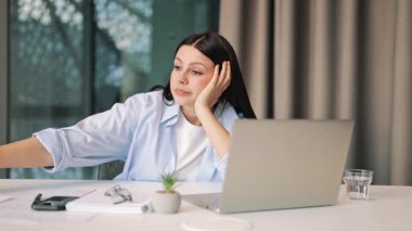 Kadın dizüstü bilgisayarla çalışırken yorgunluk ve can sıkıntısı belirtileri gösteriyor. Bunalmış hissediyor, konsantrasyonu zor buluyor, uzun süren çalışma, stres ve tükenmenin etkilerini gösteriyor. Dinlenmeye ihtiyacı var.