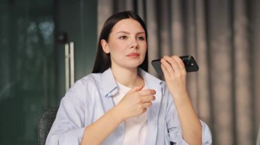 Odaklanmış kadın akıllı telefon sesi dinliyor, kulağının yanında bir cihaz tutuyor. Bilgi alırken konsantrasyon ve düşüncelilik gösterir. Modern iletişim anı.