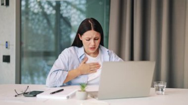 Dizüstü bilgisayar üzerinde çalışırken aniden, keskin göğüs ağrısı ve rahatsızlığı olan bir kadın. Ciddi endişe ve nefes darlığı gösteriyor. Durum için acil tıbbi müdahale gerekebilir..