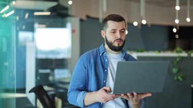 Yoğunlaştırılmış ifadeye sahip profesyonel bir adam, modern bir ofis içinde bir dizüstü bilgisayar kullanarak online bir iş görüşmesi yapıyor. Adanmışlık ve odaklanma, neredeyse amaçla işbirliği.