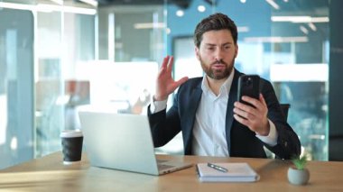 İş adamı, modern ofisten kendine güvenen iletişimini belirterek profesyonel video görüşmelerine girişiyor. Sanal toplantı sırasında ortaklarla bağlantı kurma azmi ve yenilikçi fikirler.