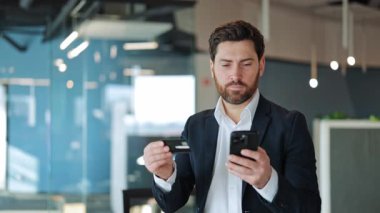 Güvenilir bir iş adamı güvenli online alışverişe girişiyor. Kredi kartı ve akıllı telefonu elinde tutmak, başarılı bir işlemden sonra tatmin olmak ve mutlu olmak. Dijital ticaret ödeme çözümleri.