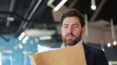 İşadamı ofiste belge okur. Yüzü endişe gösteriyor, derin üzüntü ve hayal kırıklıklarına evriliyor. Önemli bilgilerin ya da zor haberlerin duygusal etkilerini yansıtıyor.