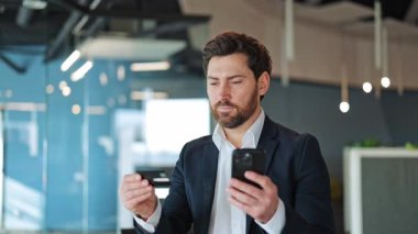 Çevrimiçi alışveriş sırasında şaşkınlık ve şaşkınlık yaşayan iş adamı, kredi kartı ve telefon kullanarak ödeme sorunuyla karşılaşır. İşlemle kaygı ve hayal kırıklığını ifade eder.