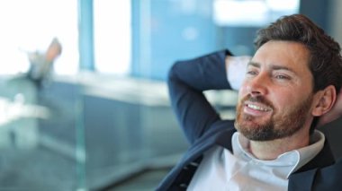 Modern ofis ortamında profesyonel iş adamı. Rahatlamış ve mutlu, bir anlık başarı ve memnuniyetin tadını çıkarıyor. Düşünceli ifade iç huzuru yansıtır, başarıyı ve refahı gösterir..