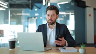 Modern ofis içinde iş adamı verimliliği. Odaklanmış bireyler dizüstü bilgisayar ve akıllı telefon kullanarak özveri ve konsantrasyon gösterir, önemli ve düşünceli bir ilişki hissi taşır..