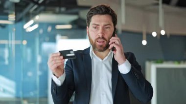 Profesyonel adam, ödeme kartı, telefon görüşmesi. Finansal tartışmalar sırasında şaşkınlık ve endişeyi ifade eder. Çevrimiçi işlem veya beklenmedik harcamalarla ilgili endişeleri yansıtır.