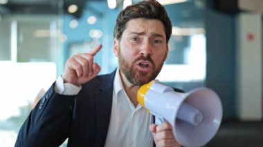 İş adamı yüksek sesle megafona bağırıyor, yoğun öfke ve hayal kırıklığını ifade ediyor. Saldırganca işaret etmek, dikkat çekmek, iş ortamında aciliyet ve güçlü hisleri iletmek..