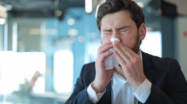 İş adamı iş yerinde soğuk algınlığı belirtileri gösterir. Burnu dokuya sümkürmek, baş ağrısından rahatsız olmak, rahatsızlık göstermek. Profesyonel çevre, hastalıkla mücadele.