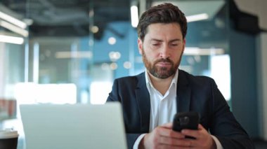 Profesyonel bir adam çağdaş bir ofis ortamında verimli çalışmak için bilgisayar ve akıllı telefon da dahil olmak üzere modern teknolojiyi kullanır. Günlük iş görevlerinde verimlilik ve bağlantı.