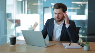 Dizüstü bilgisayarla çalışan profesyoneller, stres ve yorgunluk belirtileri gösteren ağrılı baş ağrılarıyla boğuşuyor. Modern ofis ortamında çalışmanın baskısını yansıtıyor, yorgun ve hayal kırıklığına uğramış hissediyor..