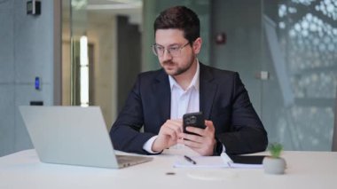 Profesyonel, dikkatli çalışıyor, akıllı telefon ve dizüstü bilgisayarla birden fazla iş yapıyor. Modern bir ofiste odaklanma, adanmışlık ve verimlilik gösteriyor..