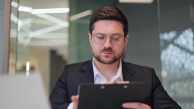 Modern ofis ortamındaki önemli belgeleri profesyonel incelemeler. Odaklanmış ve ciddi, önemli iş kararlarını düşünceli bir ifadeyle ve derin bir konsantrasyonla düşünüyor..