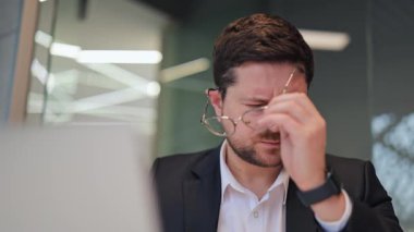 Modern ofiste çalışırken rahatsızlık ve baş ağrısı çeken bir iş adamı. Ağrı, stres ve yorgunluk belirtileri görülebilir, iş ve yorgunluk baskısı. Gerginlikten kurtulmaya ihtiyacı var..