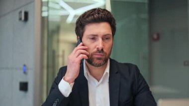 Profesyonel, çağdaş ofis içinde ciddi bir telefon görüşmesi yapıyor. Önemli ayrıntıları iletirken odaklanmayı ve kararlılığı ifade eder, konsantrasyonu iletir.