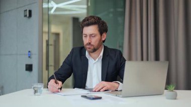 Profesyonel çalışan, çağdaş bir ofis masasında notlar alan biri. Başarı ve üretkenliği temsil ederek, iş ortamında konsantrasyon ve adanmışlığı gösterir.