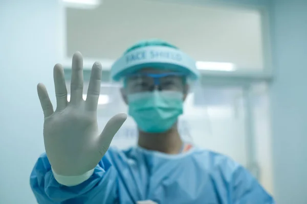 Healthcare worker wearing PPE suit for protect virus and show stop hand gesture for physical space between people to avoid spreading illness. selective focus at hand.