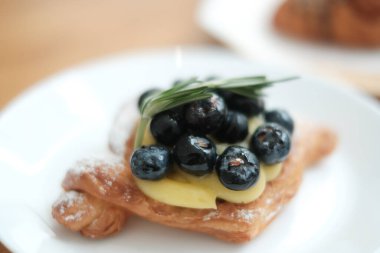 Tatlı - kirazlı kruvasan Fransız pastanesidir. Kahvehanenin masasında gevrek altın kruvasanlar çilek kreması ile dolu.
