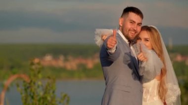 Güzel düğün çifti gelin ve damat mutlu bir gülümsemeyle başparmaklarını göster..