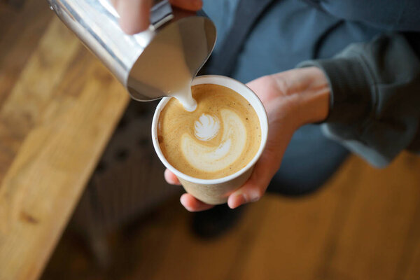 Бариста готовит капучино в бумажном стаканчике.