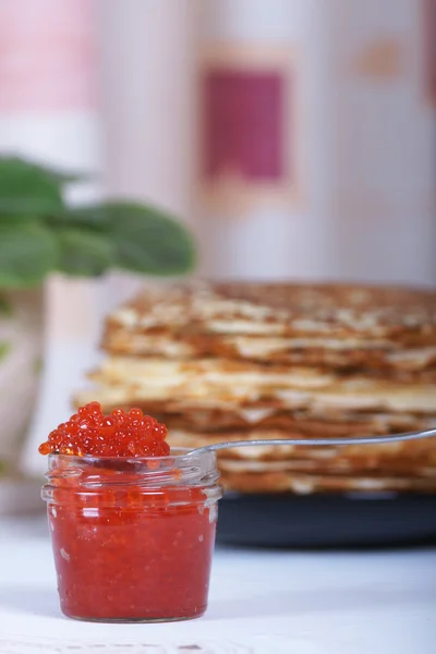 Die Bank von rotem Kaviar auf dem Hintergrund eines großen Stapels Pfannkuchen auf dem Tisch — Stockfoto