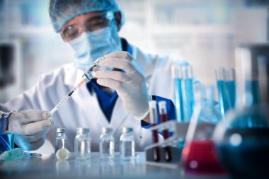 Virolog laboratuvar tezgahında aşı araştırması yapan bir şırınga dolduruyor. Yatay bileşim. Ön görünüm.