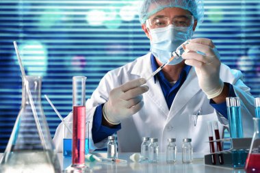 Virolog laboratuvar tezgahında aşı araştırması yapan bir şırınga dolduruyor. Yatay bileşim. Ön görünüm.