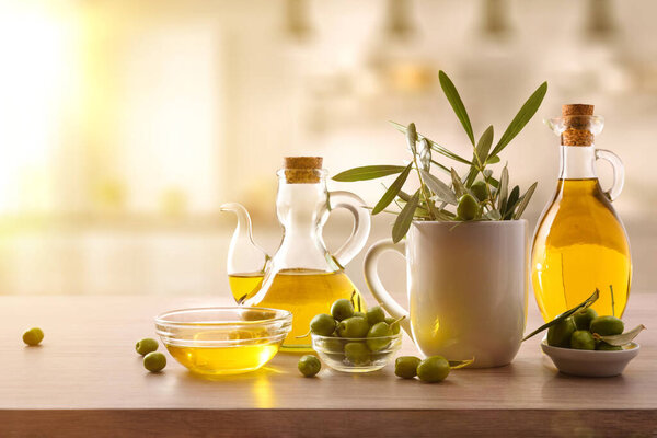 Девственное оливковое масло в двух стеклянных контейнерах и оливки собирают на деревянной скамейке на кухне. Вид спереди.