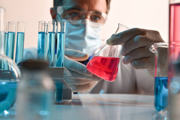 Detail of scientist manipulating carefully at a red liquid in a flask on a laboratory table. Horizontal composition. Front view.