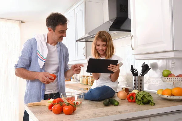 Happy father and daughter preparing vegetables to make a plate of food cooking at home with digital recipes