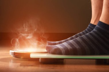 Kilo problemi olan birinin dumandan çıkan bir ölçekte tartılması fikri. Ön manzara. Yatay bileşim.