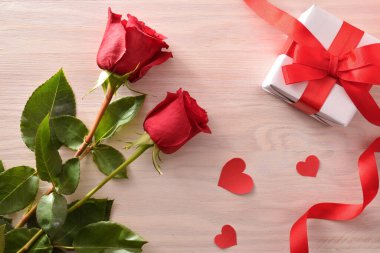 Kırmızı gül ve kırmızı kurdeleli romantik bir arkaplan, beyaz hediye kutusu, kırmızı fiyonk ve ışık. Üst görünüm.