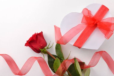 Kırmızı gül ve beyaz masa üzerinde kırmızı kalp şeklinde bir fiyonk olan beyaz hediye kutusu olan romantik bir arka plan. Üst görünüm.