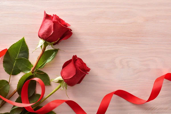 Ρομαντικό Φόντο Δύο Κόκκινα Τριαντάφυλλα Και Κόκκινη Κορδέλα Ξύλινο Τραπέζι — Φωτογραφία Αρχείου