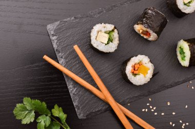 Tahta tabakta çeşit çeşit suşi maki ve siyah ahşap masada çubuklar. Üst Manzara. Yatay bileşim.