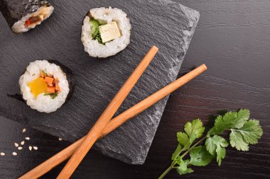 Tahta tabakta çeşit çeşit suşi maki ve siyah ahşap masada çubuklar. Üst Manzara. Yatay bileşim.