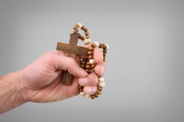 Kafkas dindar bir adamın eli inançla sıkıca sarılmış koyu kahverengi bir haç ve ahşap kolye ile izole edilmiş gri arka planda dua etmek için.