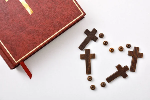 Background with bible and heart made with crosses and beads on white table. Horizontal composition. Top view