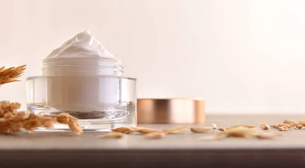 Oat body and facial moisturizer cream in glass jar with spikes on wooden table with beige isolated background